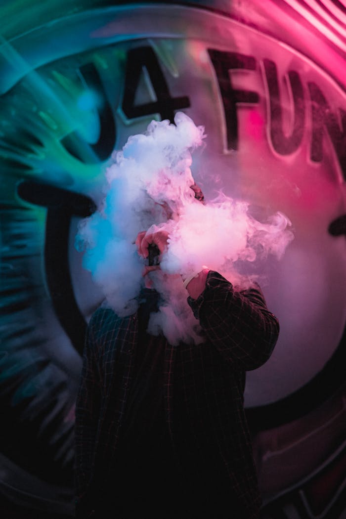 Home Person exhaling smoke in front of colorful neon graffiti, creating a mysterious urban vibe.